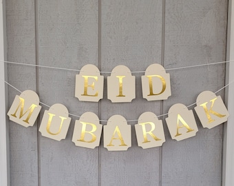 May include: A beige banner with gold letters spelling "Eid Mubarak".