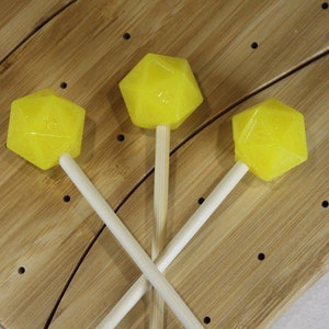 May include: Three yellow lollipops on wooden sticks, arranged in a triangular pattern on a wooden surface.