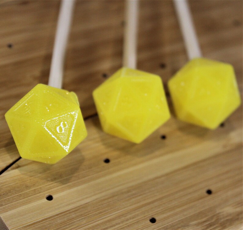 May include: Three yellow, candy-like dice on sticks. The dice are shaped like a twenty-sided die, also known as a d20.