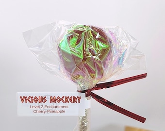 May include: A lollipop with a holographic wrapper and a red ribbon. The label reads "Vicious Mockery, Level 2 Enchantment, Cherry-Pineapple". The candy is on a clear stick.