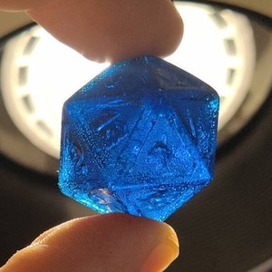 Puede incluir: Un dado de 20 caras de vidrio azul con una superficie texturizada.