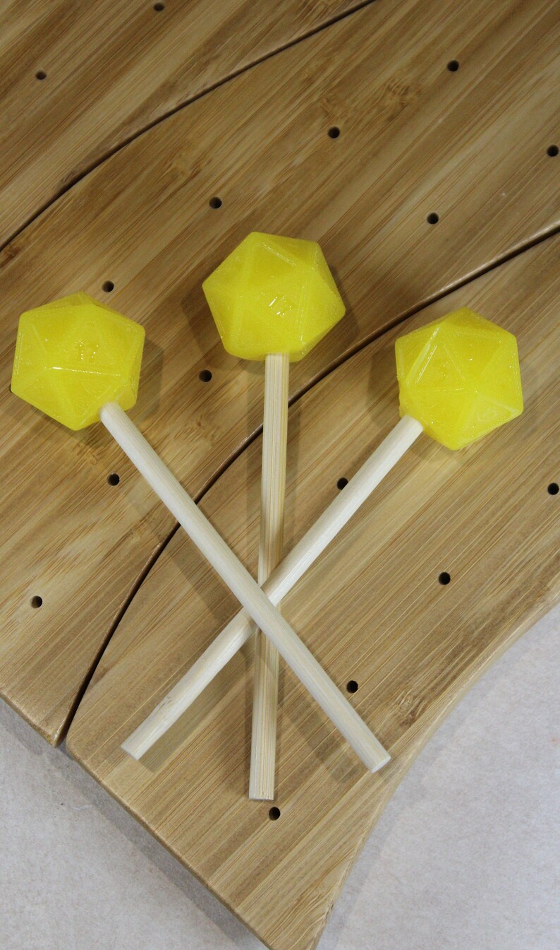 May include: Three yellow lollipops on wooden sticks, arranged in a triangular pattern on a wooden surface.