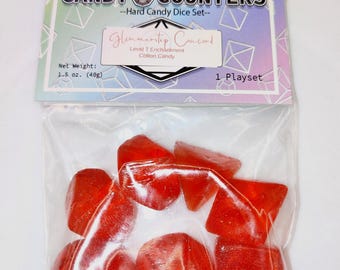 May include: A clear plastic bag containing red, hard candy dice. The bag is labeled "Candy Counters - Hard Candy Dice Set" with "Glimmeritep Concord" and "Cotton Candy" text. The net weight is 1.5 oz (40g).