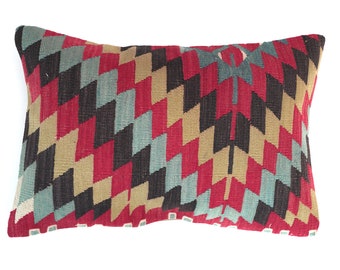 May include: A rectangular pillow with a geometric pattern in shades of red, black, beige, and teal. The pattern is made up of repeating triangles and zigzags.