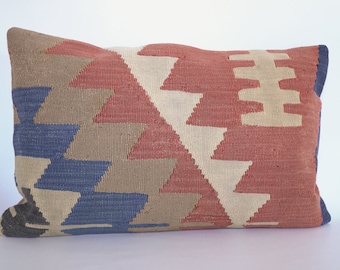 May include: A rectangular pillow with a geometric pattern in shades of red, brown, blue, and white. The pillow is made of woven fabric and has a fringed edge.