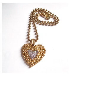 May include: A gold heart-shaped pendant necklace with a smaller heart-shaped design in the center, set with clear rhinestones. The necklace is on a gold ball chain.