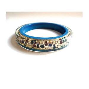Könnte beinhalten: Ein blaues Armband mit einem goldenen Band und bunten Akzenten. Das Armband ist mit einem Muster aus kleinen, bunten Punkten und Wirbeln verziert.