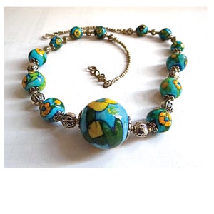 Pode incluir: Um colar de contas de cerâmica azul turquesa e amarelo com padrões florais e uma conta grande, redonda, azul turquesa e amarela com padrões florais no centro. O colar é feito de contas de cerâmica e metal prateado.