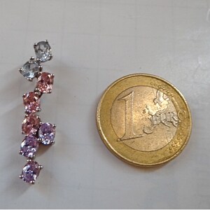 May include: A silver earring with a cluster of pink, purple, and blue oval-shaped gemstones. The earring is about the size of a US one euro coin.