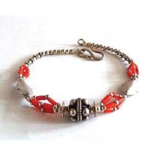 Op de afbeelding: Een zilveren armband met rode koraal kralen en een zilveren sluiting. De armband heeft een zilveren kraal met een getextureerd ontwerp in het midden.