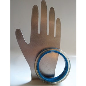 Pu&ograve; includere: Un supporto a forma di mano argentato con un braccialetto blu e argento.