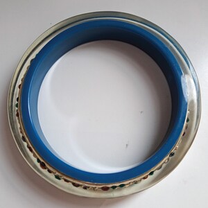 Pu&ograve; includere: Un braccialetto in plastica trasparente con una fascia blu e un bordo dorato e multicolore.