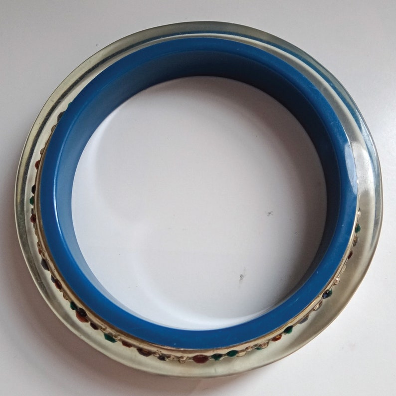 Pu&ograve; includere: Un braccialetto in plastica trasparente con una fascia blu e un bordo dorato e multicolore.