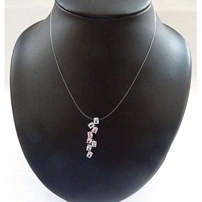 May include: A delicate necklace with a clear, thin chain and a pendant featuring a cluster of pink and blue gemstones. The pendant is shaped like a teardrop and the gemstones are arranged in a cascading pattern.