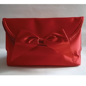 May include: A red satin clutch bag with a large bow and a YSL logo.