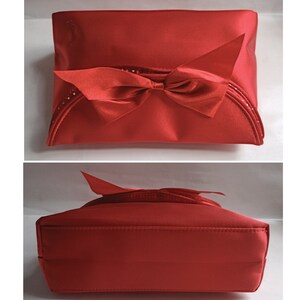 May include: Red satin cosmetic bag with a large red satin bow. The bag has a white dotted trim around the edges.