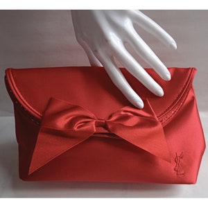 May include: A red satin clutch with a large red satin bow and the Yves Saint Laurent logo.