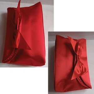 May include: A red satin makeup bag with a large satin bow and a row of rhinestones. The bag is closed and the bow is tied in a knot.