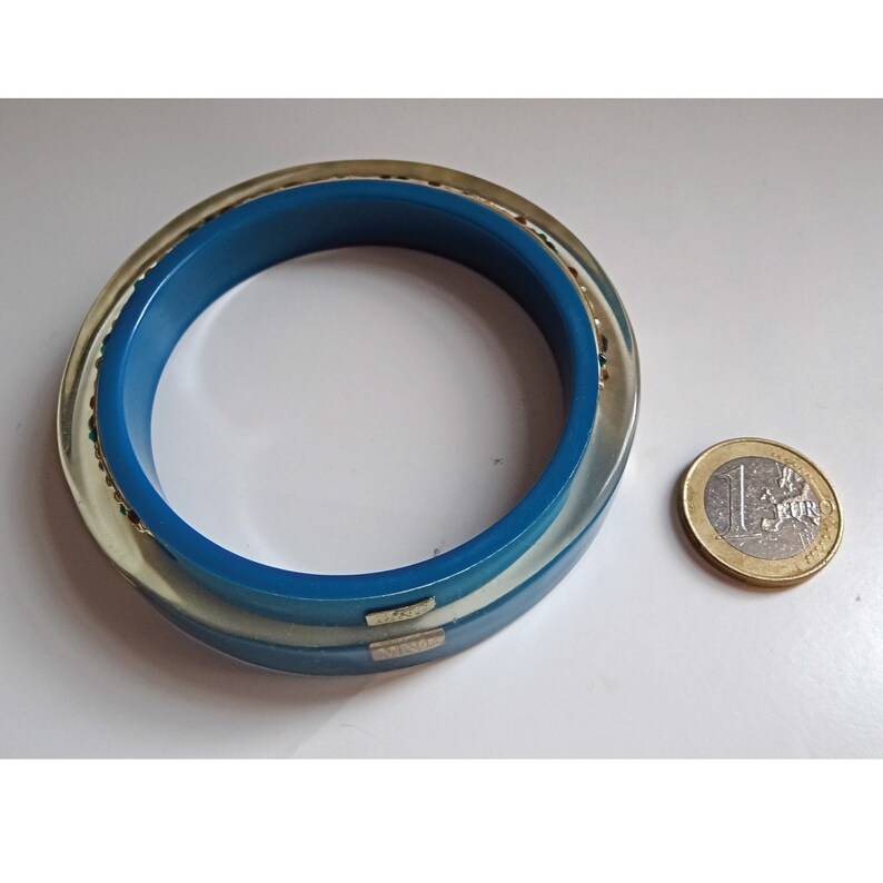 Pu&ograve; includere: Un braccialetto blu e bianco con un bordo dorato scintillante. Il braccialetto &egrave; circa delle dimensioni di una moneta da un euro.