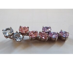 May include: A silver charm bracelet with a gradient of blue, pink, and purple gemstones. The charm bracelet features a variety of round and square-shaped gemstones.