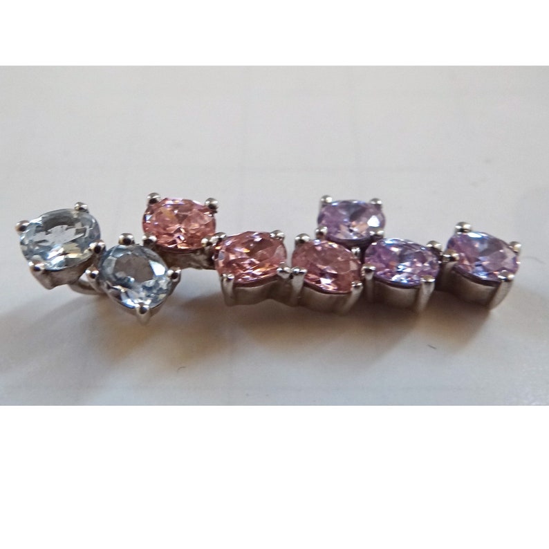 May include: A silver charm bracelet with a gradient of blue, pink, and purple gemstones. The charm bracelet features a variety of round and square-shaped gemstones.