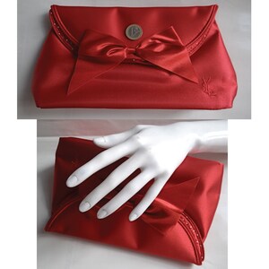 May include: A red satin clutch with a large bow and a small circular emblem. The clutch has a beaded trim and a YSL logo.