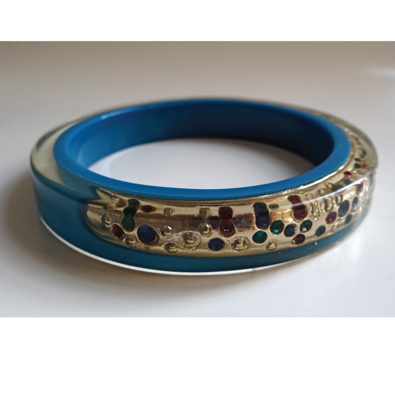 Pu&ograve; includere: Un braccialetto turchese con una fascia dorata e strass colorati.