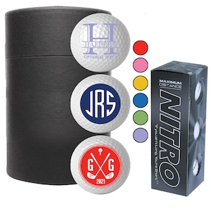 May include: A set of three personalized golf balls in a black tube. The golf balls feature different designs, including a monogram, a name with optional text, and a golf club graphic. The golf balls are packaged in a black box with the word "NITRO" printed on it.