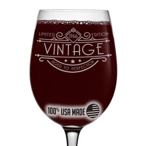 May include: A clear wine glass filled with red liquid. The glass has white text that reads "VINTAGE 1966 LIMITED EDITION AGED TO PERFECTION." Below the text is "100% USA MADE" with an American flag graphic.