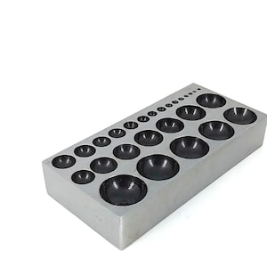 May include: A metal tool with a rectangular base and multiple round depressions of varying sizes. The depressions are black and appear to be made of a different material than the base.