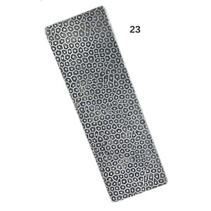 May include: A rectangular, silver-coloured metal piece featuring a textured, honeycomb-like pattern. The number "23" is printed in black in the upper right corner. It is likely a component of jewellery or a decorative element.