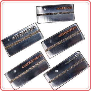 Op de afbeelding: Een verzameling van vijf rechthoekige metalen geldclips. Elke clip heeft een geborstelde zilveren afwerking met decoratieve koper- of zilverkleurige accenten. De ontwerpen omvatten gegraveerde patronen en een centrale balk. Nummers 6, 7, 8, 9 en 10 zijn zichtbaar.