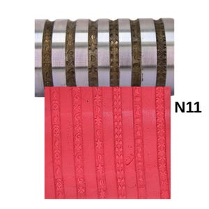 May include: A metal rolling pin with etched decorative patterns is shown above a red clay surface with matching embossed designs. The patterns include stars, moons, and floral motifs. The text "N11" is visible on the right side.