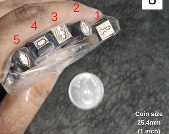 May include: Five small metal stamps with different designs, including a leaf, a bird, a butterfly, a flower, and a geometric pattern. The stamps are held in a clear plastic bag. A coin is shown for size reference, measuring 1 inch in diameter.