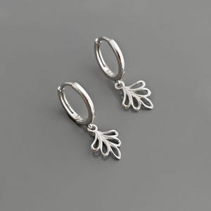 May include: A pair of silver hoop earrings with a delicate leaf-shaped dangle charm. The earrings are simple and elegant, perfect for everyday wear.