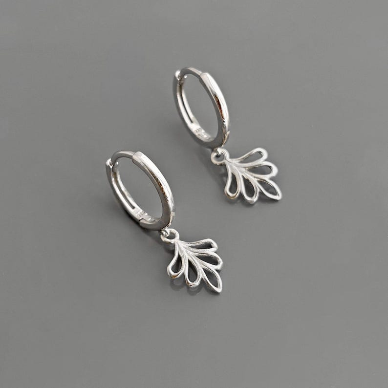 May include: A pair of silver hoop earrings with a delicate leaf-shaped dangle charm. The earrings are simple and elegant, perfect for everyday wear.