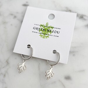 May include: Silver hoop earrings with a delicate leaf design dangle from the hoops. The earrings are displayed on a white card with the text "Vintage Made Modern Green Bijou www.greenbijou.com"