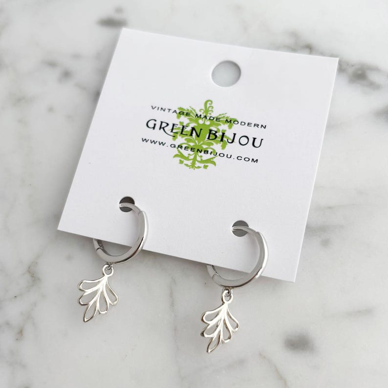 May include: Silver hoop earrings with a delicate leaf design dangle from the hoops. The earrings are displayed on a white card with the text "Vintage Made Modern Green Bijou www.greenbijou.com"