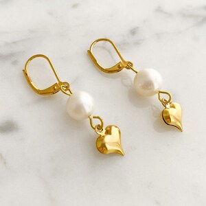 Pode incluir: Brincos de ouro com uma p&eacute;rola e um pingente em forma de cora&ccedil;&atilde;o.