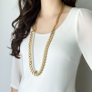 May include: A gold chain necklace with a strand of white pearls. The necklace is layered and features a chunky gold chain and a delicate pearl strand.
