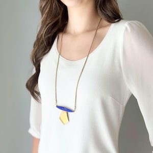 May include: A long gold-tone chain necklace with a blue and gold pendant. The blue portion of the pendant is oval-shaped with a white starburst design. The gold portion is a geometric shape.