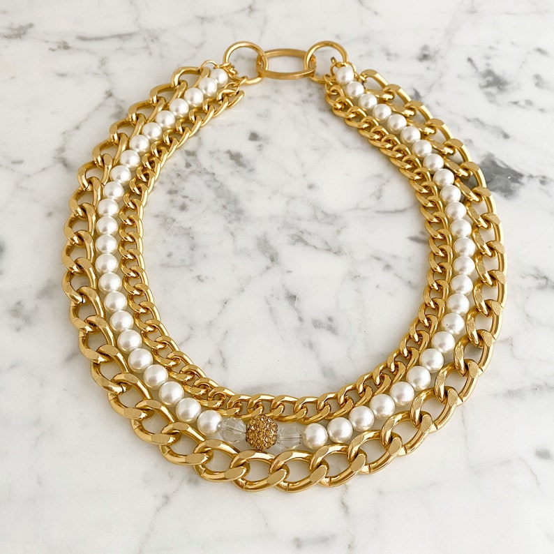 May include: A gold chain necklace with a double strand of faux pearls. The necklace has a small gold accent in the center.