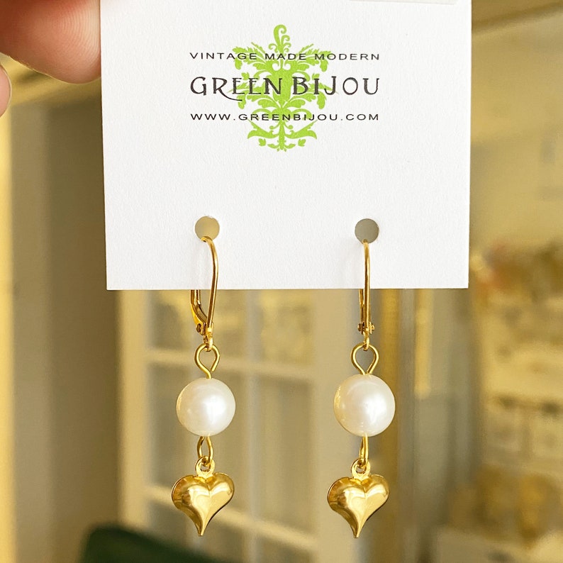 Pode incluir: Brincos de cora&ccedil;&atilde;o de ouro com um pingente de p&eacute;rola branca. Os brincos est&atilde;o em um cart&atilde;o branco com o texto "Vintage Made Modern Green Bijou www.greenbijou.com"