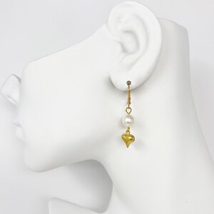 Pode incluir: Brincos de argola dourados com uma &uacute;nica p&eacute;rola branca e um pingente de cora&ccedil;&atilde;o dourado.