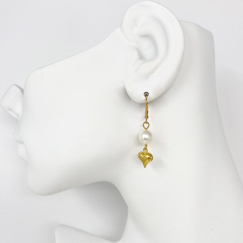 Pode incluir: Brincos de argola dourados com uma &uacute;nica p&eacute;rola branca e um pingente de cora&ccedil;&atilde;o dourado.