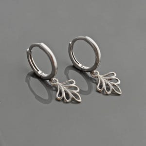 May include: A pair of silver hoop earrings with a delicate leaf-shaped dangle charm.