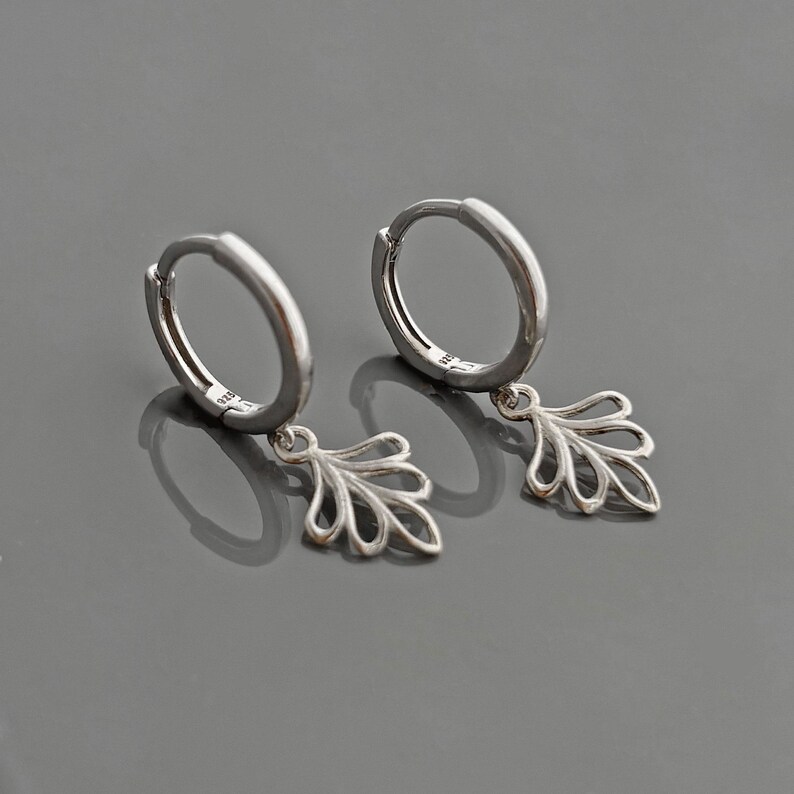 May include: A pair of silver hoop earrings with a delicate leaf-shaped dangle charm.