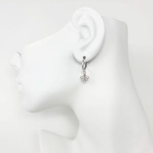 May include: Silver hoop earrings with a delicate, fan-shaped charm dangling from each hoop.