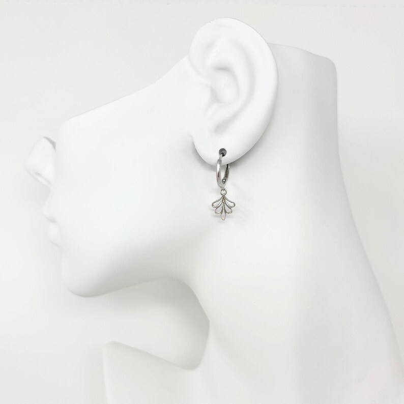 May include: Silver hoop earrings with a delicate, fan-shaped charm dangling from each hoop.
