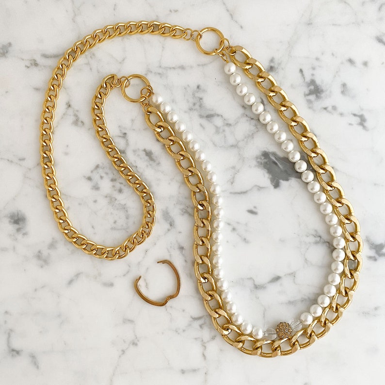 May include: A gold chain necklace with a double strand of pearls. The necklace has a small gold charm with a clear crystal in the center.